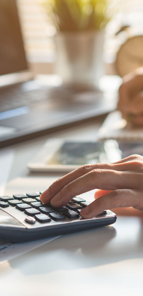Hand auf Rechner vor Blättern mit Tabellen